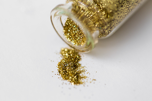 party, decoration and holidays concept - close up of golden glitters poured from small glass bottle over white background