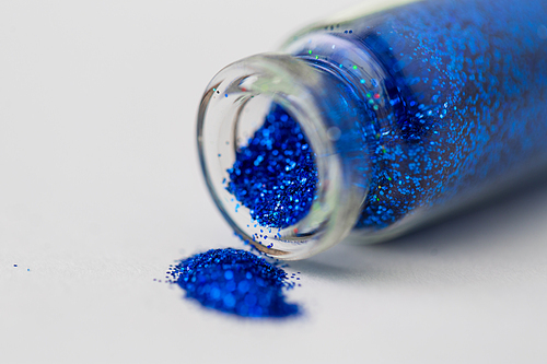 party, decoration and holidays concept - close up of ultramarine blue glitters poured from small glass bottle over white background