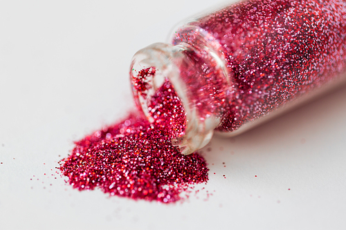 party, decoration and holidays concept - close up of pink red glitters poured from small glass bottle over white background