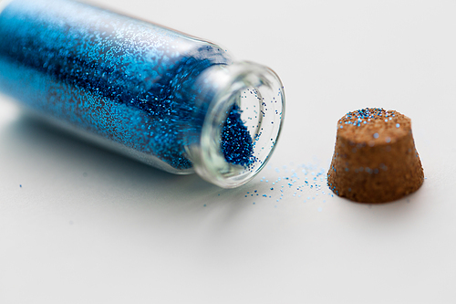 party, decoration and holidays concept - close up of blue glitters in small glass bottle with cork stopper over white background