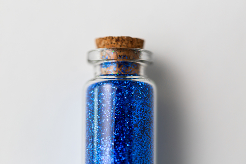 party, decoration and holidays concept - close up of ultramarine blue glitters in small glass bottle with cork stopper over white background