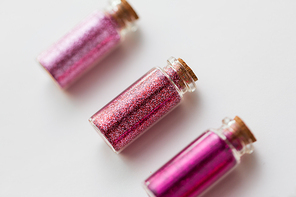 party, decoration and holidays concept - close up of glitters of different red and pink shades in small glass bottles with cork stoppers over white background