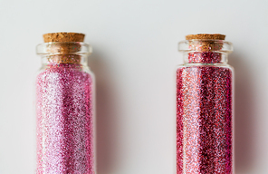 party, decoration and holidays concept - close up of glitters of different red and pink shades in small glass bottles with cork stoppers over white background