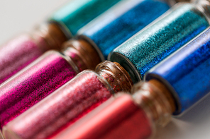 party, decoration and holidays concept - close up of different color glitters in small glass bottles with cork stoppers over white background