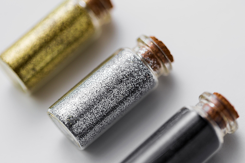 party, decoration and holidays concept - close up of gold, silver and black metallic glitters in small glass bottles with cork stoppers over white background