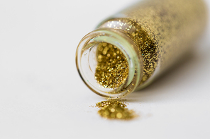 party, decoration and holidays concept - close up of golden glitters poured from small glass bottle over white background