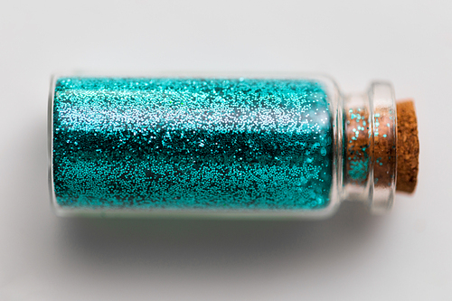 party, decoration and holidays concept - blue glitters in small glass bottle with cork stopper over white background