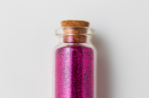 party, decoration and holidays concept - close up of fuchsia pink glitters in small glass bottle with cork stopper over white background