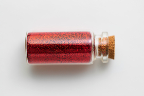 party, decoration and holidays concept - red glitters in small glass bottle with cork stopper over white background