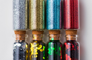 party, decoration and holidays concept - close up of different color glitters in small glass bottles with cork stoppers over white background