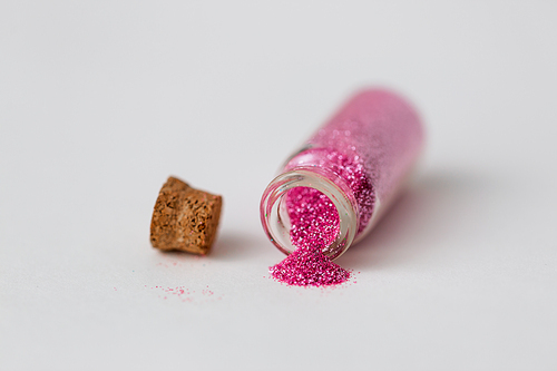 party, decoration and holidays concept - pink glitters poured from small glass bottle and cork over white background