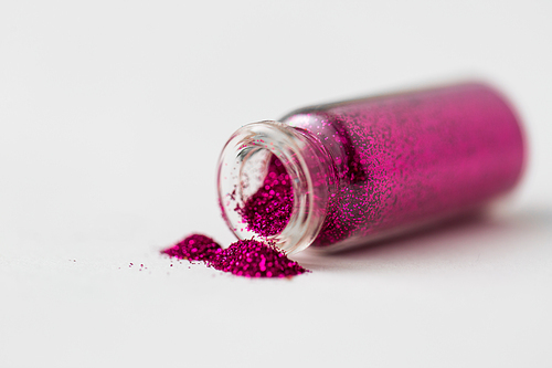 party, decoration and holidays concept - fuchsia pink glitters poured from small glass bottle over white background