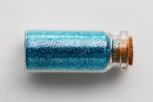 party, decoration and holidays concept - blue glitters in small glass bottle with cork stopper over white background