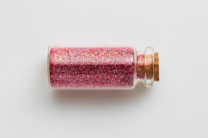 party, decoration and holidays concept - red glitters in small glass bottle with cork stopper over white background