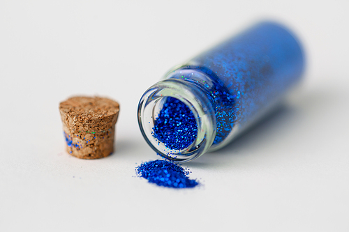 party, decoration and holidays concept - close up of ultramarine blue glitters poured from small glass bottle and cork stopper over white background