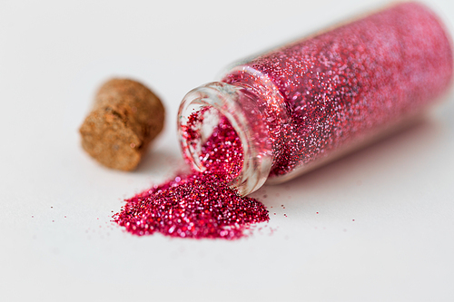 party, decoration and holidays concept - close up of pink red glitters poured from small glass bottle and cork over white background