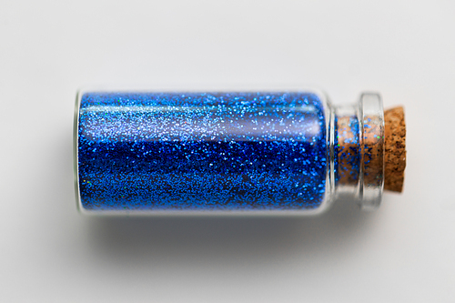 party, decoration and holidays concept - ultramarine blue glitters in small glass bottle with cork stopper over white background