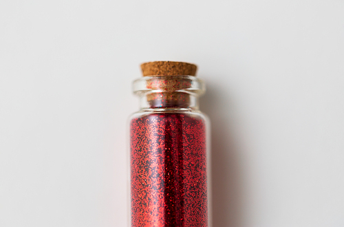 party, decoration and holidays concept - close up of red glitters in small glass bottle with cork stopper over white background