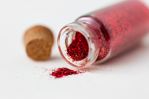 party, decoration and holidays concept - close up of red glitters poured from small glass bottle and cork over white background