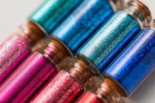 party, decoration and holidays concept - close up of different color glitters in small glass bottles with cork stoppers over white background