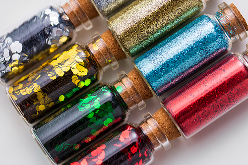party, decoration and holidays concept - close up of different color glitters in small glass bottles with cork stoppers