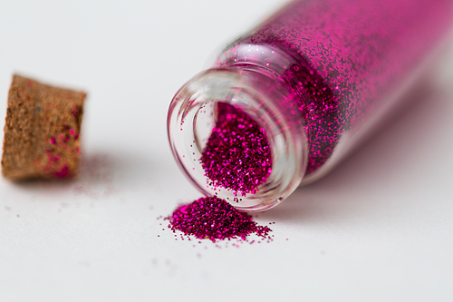 party, decoration and holidays concept - close up of fuchsia pink glitters poured from small glass bottle and cork over white background