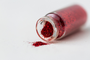 party, decoration and holidays concept - close up of red glitters poured from small glass bottle over white background