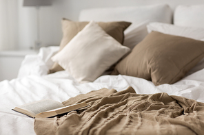comfort, hygge and interior concept - cozy bed with pillows, blanket and open book at home