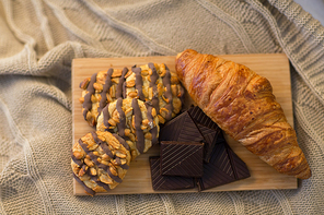 food, eating and breakfast concept - croissant, chocolate pieces and cookies on wooden board