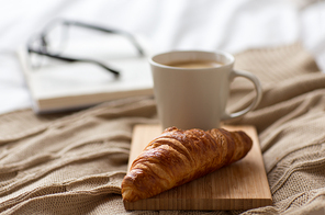 food, eating and breakfast concept - croissant and cup of coffee on bed at cozy home