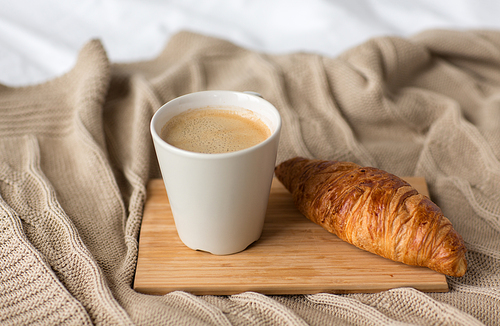 food, eating and breakfast concept - cup of coffee and croissant on bed or blanket at cozy home