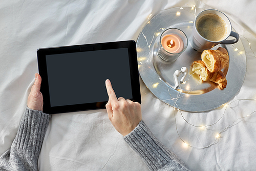 technology, hygge and christmas concept - hands of woman with tablet pc computer, croissant and coffee in bed