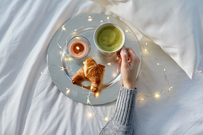 food, breakfast and people concept - hand of woman drinking coffee with croissant in bed