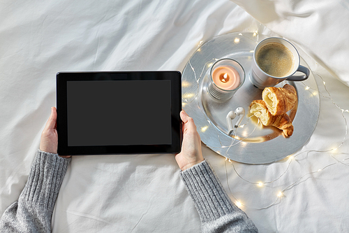 technology, hygge and christmas concept - hands of woman with tablet pc computer, croissant and coffee in bed