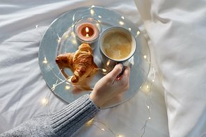 food, breakfast and people concept - hand of woman drinking coffee with croissant in bed
