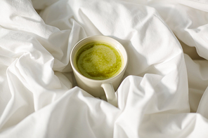 morning, hygge and drink concept - cup of matcha tea in bed at home