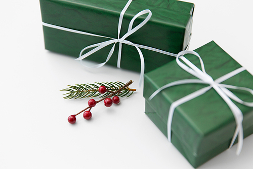 winter holidays, new year and christmas concept - gift boxes wrapped into green paper and fir tree branch with red berries on white background