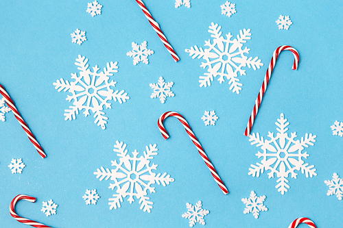 christmas, snow and winter holidays concept - white snowflakes and candy cane decorations on blue background