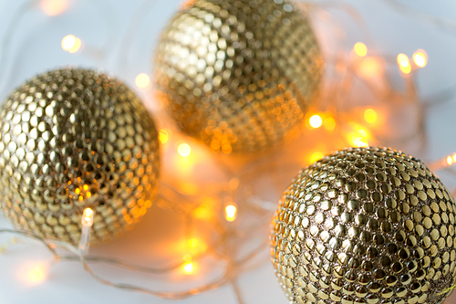 decoration, holidays and luxury concept - golden christmas balls and garland lights