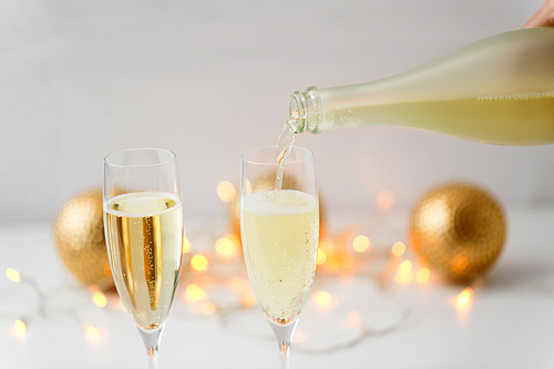 christmas, holidays and celebration concept - close up of champagne pouring from bottle to glasses