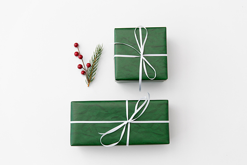 winter holidays, new year and christmas concept - gift boxes wrapped into green paper and fir tree branch with red berries on white background