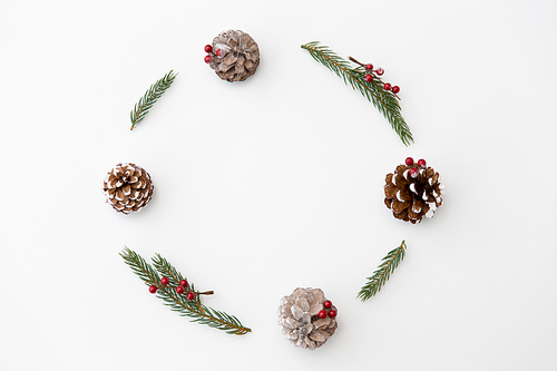 winter holidays, new year and decorations concept - frame of fir branches with red berries and pine cones on white background