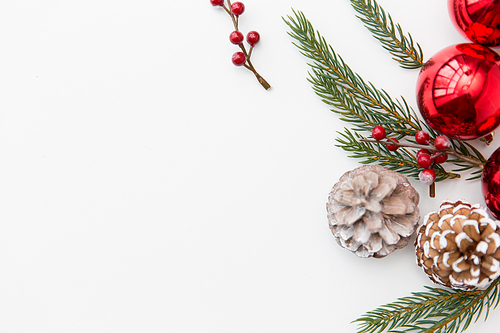 winter holidays, new year and decorations concept - red christmas balls and fir branches with pine cones on white background