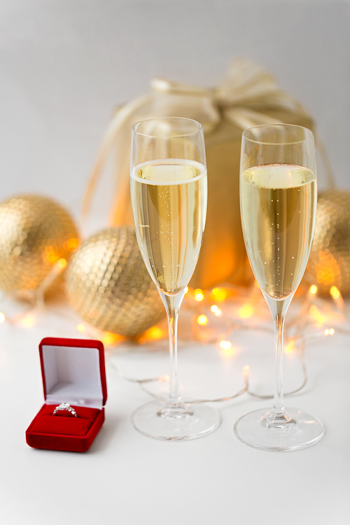 christmas, holidays and celebration concept - glasses of champagne and diamond ring in little red gift box