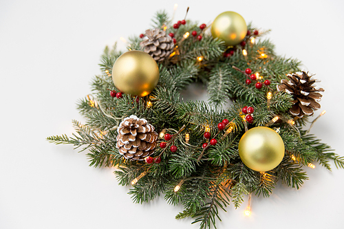 winter holidays, new year and decorations concept - wreath of fir branches with golden balls, pine cones and garland lights on white background