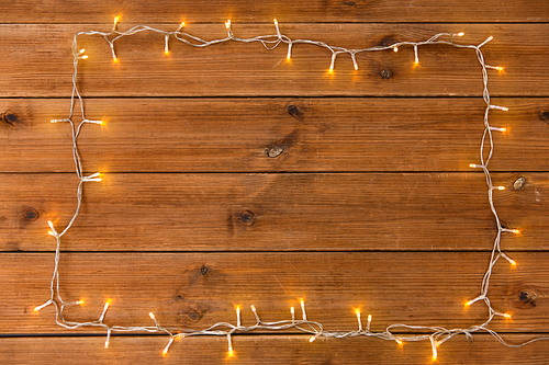 christmas, holidays and illumination concept - frame of electric garland lights on wooden background