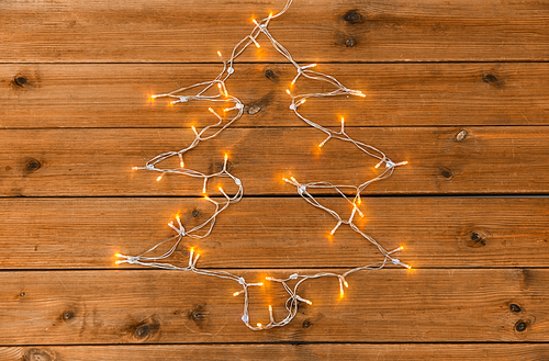 holidays and illumination concept - electric garland lights string in shape of christmas tree on wooden background
