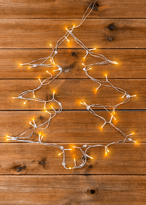 holidays and illumination concept - electric garland lights string in shape of christmas tree on wooden background