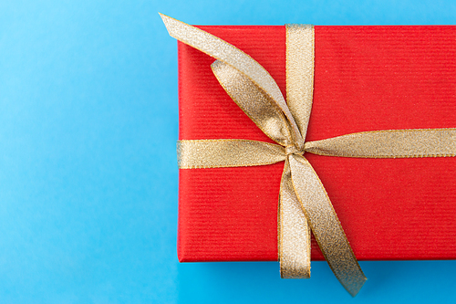 holiday, greeting and surprise concept - christmas red gift box with golden bow on blue background