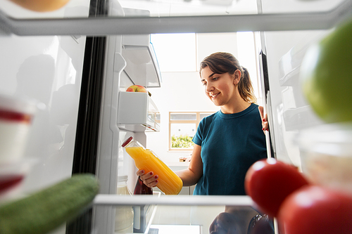 healthy eating, food and diet concept - happy woman taking bottle of orange juice from fridge at home kitchen